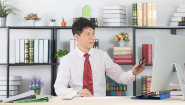 Onun çalışma alanı başlangıç ofis, bilgisayar ve ofis arka plan ile çalışan orta yaşlı, yakışıklı, Asya, işadamı, koyu kırmızı kravat, Beyaz gömlekli portresi,