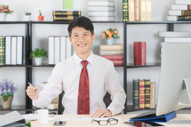Mutlu orta yaşlı, yakışıklı, Asyalı, işadamı, beyaz gömlek, koyu kırmızı kravat, gülümseyen, onun başlangıç ofisinde çalışan, bilgisayar ve ofis arka plan ile,