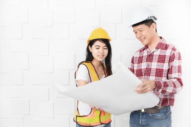 Kask, blueprint kontrol portakal, sarı yansıtıcı Emanet yelek ve kask, giyen genç kadın Asya asistanı, öğretim giyen orta yaşlı Asya mimar, kot pantolon ve ekose desenli gömlek,