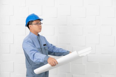 Orta yaşlı, Asya elektrikçi veya içinde tulum, üniforma, giyiyor mavi emniyet kask, çalışma İnşaat çizim, taslakları, beyaz ofis arka planda çalışan teknisyeni varoluş portresi