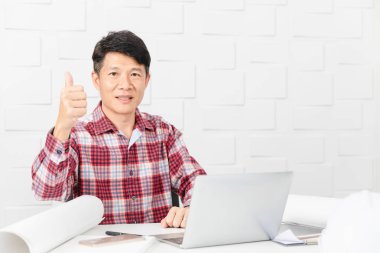 Jest, yukarı arka planda iş ilerleme ile dizüstü bilgisayar, tablet ve belgeler ile memnun yapım inşaat site ofiste çalışan Asya yakışıklı mimar, ekose desenli gömlek, orta yaşlı