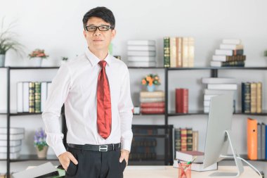 Doğrudan kameraya bakarak onun çalışma alanı başlangıç ofisinde önünde poz gözlük, beyaz gömlek, koyu kırmızı kravat giyiyor orta yaşlı, yakışıklı, Asya, işadamı, portresi