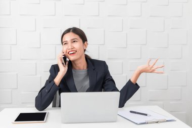 Genç güzel, Asyalı iş kadını, koyu iş elbisesi içinde, sürpriz ile meslektaşı ile konuşurken, rahatsız ifade, dizüstü bilgisayar, tablet, not defteri, kalem ve beyaz tuğla duvar panosu oda arka plan