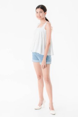 Stüdyo portre rahat yaz kıyafetler, kot şort ve gevşek kolsuz bluz, geniş bir gülümseme, genç güzel, çekici Asya kadının ayakta, izole beyaz arka plan üzerinde poz