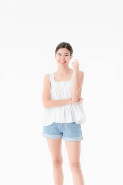 Stüdyo portre rahat yaz kıyafetler, kot şort ve gevşek kolsuz bluz, geniş bir gülümseme, genç güzel, çekici Asya kadının ayakta, izole beyaz arka plan üzerinde poz