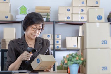 Ev ofisinde kontrol siparişleri online müşteriler ile barkod makinesi kullanarak eski Asyalı kadın. Ana temel iş ve başlangıç mülkiyeti için kavram.