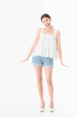 Stüdyo portre rahat yaz kıyafetler, kot şort ve gevşek kolsuz bluz, geniş bir gülümseme, genç güzel, çekici Asya kadının ayakta, izole beyaz arka plan üzerinde poz