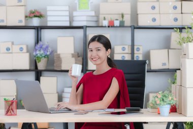 İş istasyonunda oturan yüz, gülümseyen genç güzel, çekici Asya işkadını Kırmızı elbiseli portresi e-postalar, modern başlangıç office arka plan denetimi sırasında kahve sabah fincan keyfini çıkarın