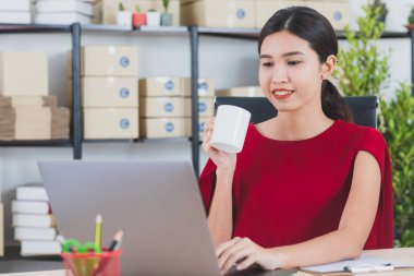 İş istasyonunda oturan yüz, gülümseyen genç güzel, çekici Asya işkadını Kırmızı elbiseli portresi e-postalar, modern başlangıç office arka plan denetimi sırasında kahve sabah fincan keyfini çıkarın