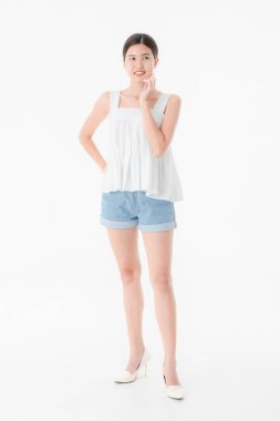 Stüdyo portre rahat yaz kıyafetler, kot şort ve gevşek kolsuz bluz, geniş bir gülümseme, genç güzel, çekici Asya kadının ayakta, izole beyaz arka plan üzerinde poz