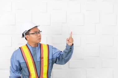 Tulum, orta yaşlı, Asya sitesi mühendisi Toplantı salonunun inşaat sahasında içinde kask ve turuncu, sarı yansıtıcı Emanet, yeleği varoluş yukarı doğru beyaz duvar arka plan işaret