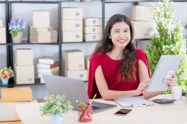 Yüzü gülen, iş istasyonunda oturan, müşteri siparişi listesi tablet, modern başlangıç office arka planda kontrol genç güzel, çekici Asya işkadını Kırmızı elbiseli portresi