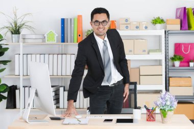 Genç, yakışıklı, portresi gözlük, takım elbise giyen Asya, işadamı, sıkıca ellerini masaya, tablet, not defteri, başlangıç office arka plan ile fotoğraf gülümseyen koy