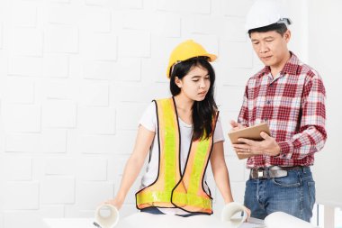 Veri üstünde laptop genç kadın Asya Yardımcısı gösterilen, portakal, sarı yansıtıcı Emanet yelek ve kask, planları elinde giyen orta yaşlı Asya mimar, kot pantolon ve ekose desenli gömlek,