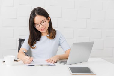 Genç, güzel, Asya mimar, giyen gözlük Oda kalem elinde, Toplantı inşaat sahasında alarak not notepad, defter ile üzerinde çalışma tablet ve smartphone ve kahve Kupası arka plan