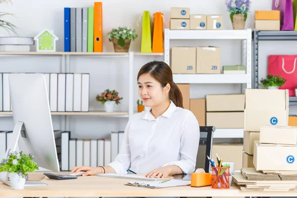 Midilli kuyruklu, beyaz tişörtlü, bilgisayarın önünde oturan, gülümseyen yüzlü, müşterilerden ve tedarikçilerden gelen e-postaları kontrol eden yakışıklı, çekici Asyalı iş kadını.