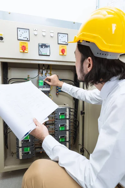 Genç Asyalı elektrik mühendisi bej pantolon ve beyaz gömlek, yakın çekim, Sarı kask, öğretim el çalışma Denetim Masası bodur takmak, onun rutin günlük kontrol izleyin