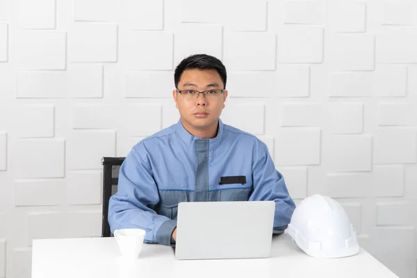 建設現場の小さなオフィスで働く中高年のアジアサイトエンジニアの肖像画 ノートパソコンのデータの入力とチェック コーヒーカップと安全帽子 青写真の背景のロール — ストック写真