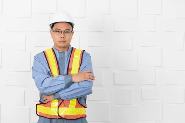 半长的中年 亚洲工地工程师在工作服 戴着头盔 黄色反光安全背心 站在建筑工地的会议室 双臂交叉 白色墙的背景 — 图库照片
