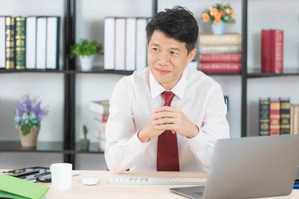 Orta yaşlı, yakışıklı, Asya, işadamı, beyaz gömlek, koyu kırmızı kravat, başlangıç ofisinde oturan eller, çalışma masası, dizüstü bilgisayar ve kahve Kupası arka plan üzerinde gururla poz geçti