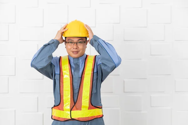 Half-length of middle aged, Asian site engineer in overalls, wearing orange, yellow reflective safety vest, in meeting room at construction site, put on yellow safety helmet, prepare for going out