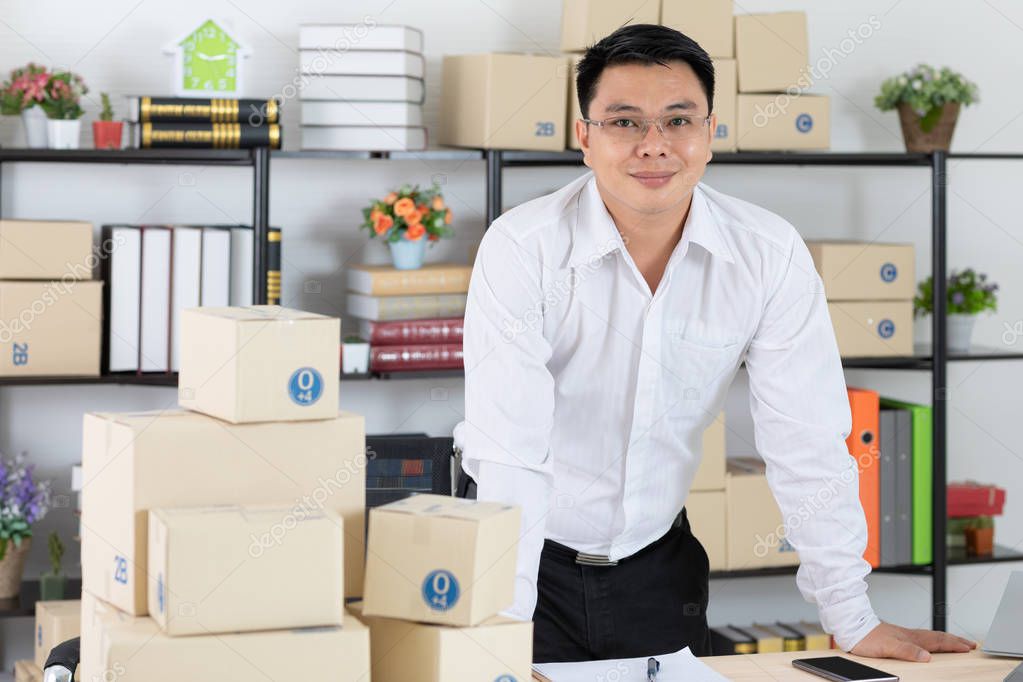 Middle aged Asian, businessman, wearing eyeglasses, white shirt, stand at his work station, at his office, smiling, pleased and confident at his achievement on startup business, office background