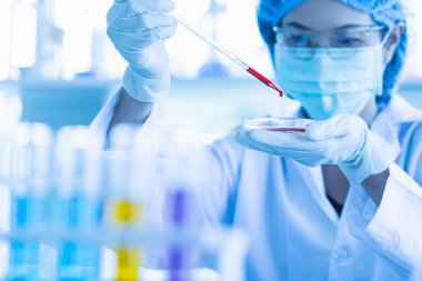 Kadın bilim adamı kırmızı sıvıyı kabın içine düşürüyor