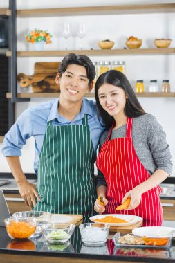  Asian couple in apron poses to camera in kitchen