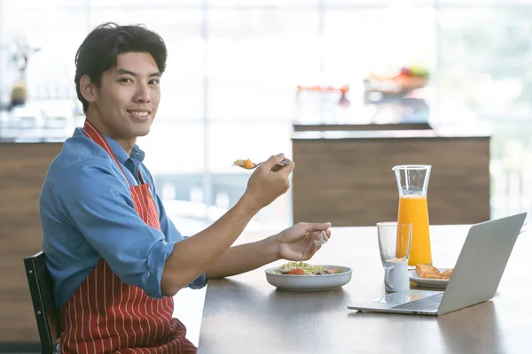 Asian man eating salad in kitchen.