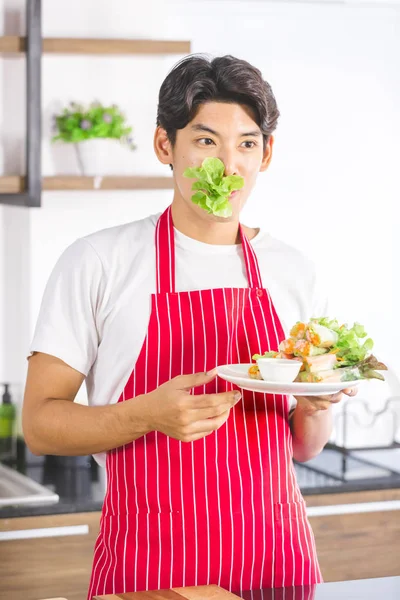 Homem asiático come salada no balcão da cozinha — Fotografia de Stock