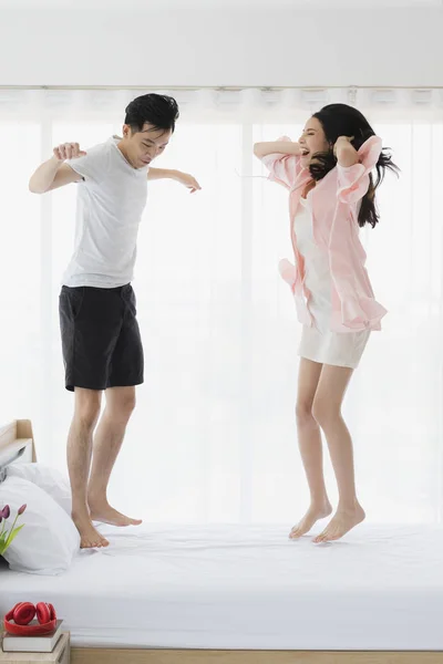 Lovely Asian couple jumping on bed in bedroom — Stock Photo, Image