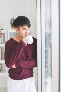 Adam ayakta ve pencerenin yanında kahve içiyor.