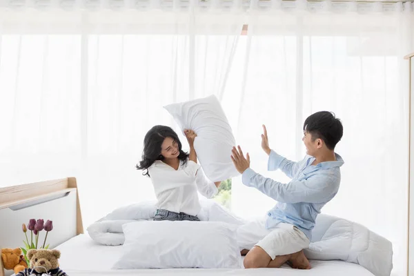 Asiática pareja se sienta en la cama, Ellos tienen almohada lucha —  Fotos de Stock