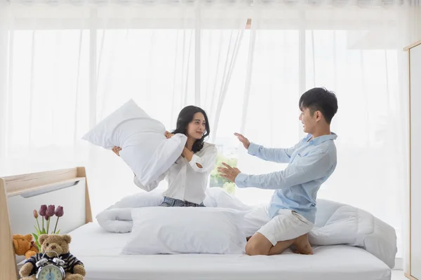 Asiática pareja se sienta en la cama, Ellos tienen almohada lucha —  Fotos de Stock