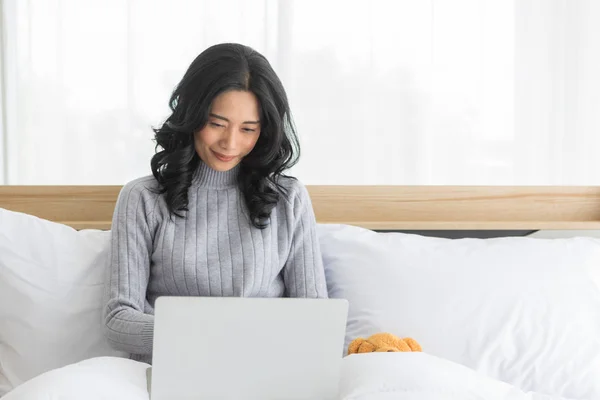 Mujer asiática sentada y usando portátil en el dormitorio . — Foto de Stock