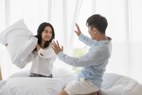 Asiática pareja se sienta en la cama, Ellos tienen almohada lucha —  Fotos de Stock