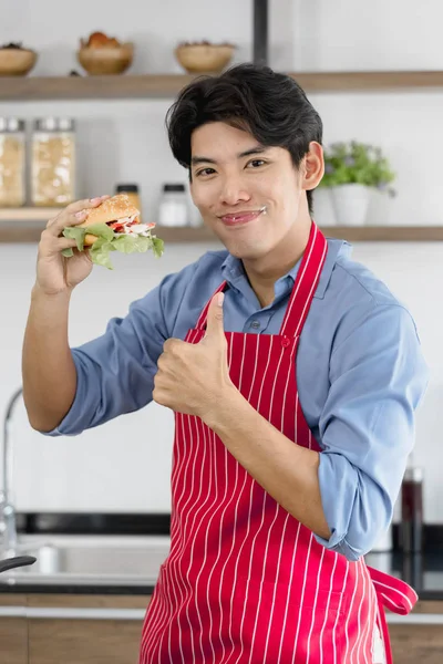 Asiático hombre, él sostiene un hamburguesa y golpes hasta —  Fotos de Stock