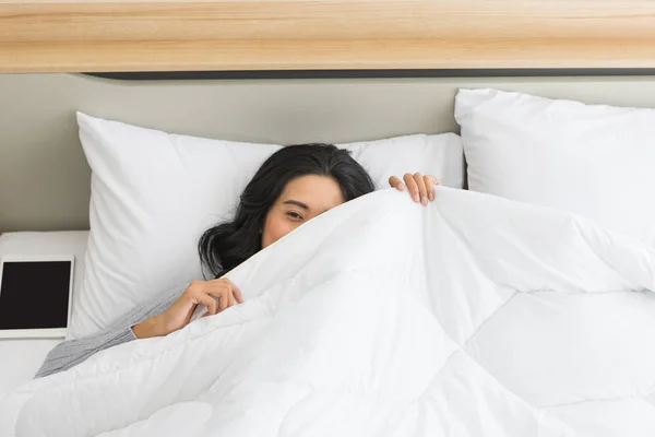 Vrouw liggend in bed en kijkend over de deken — Stockfoto