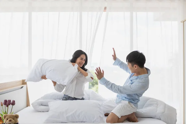 Asian couple sits on bed, They have pillow fight