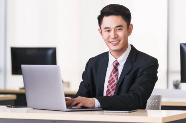 Asyalı işadamı gülümseyerek ve ofiste oturarak