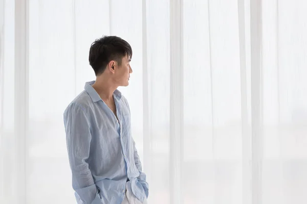 Asiático homem fica na frente da janela no quarto — Fotografia de Stock