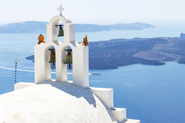 Views of the volcanic island Tholos along the clock tower of a chapel in Fira, Santorini, Greece