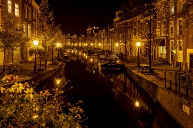 Oude Rijn 'deki Sint Jansbrug' dan bir gece çekimi. Çok sayıda tekne ve eski kanal kenarındaki evleri aydınlatan Leiden, Hollanda