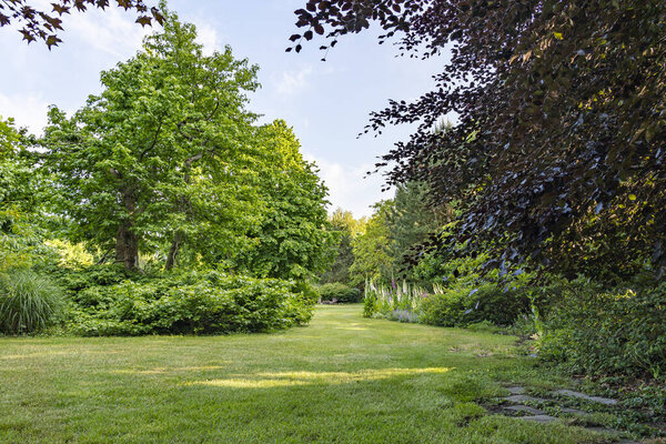 The lawn meanders between the various bushes with trees in a multitude of leaf shades in this beautifully landscaped garden with a great diversity of trees and flowering shrubs near the village of Harkstede in Groningen
