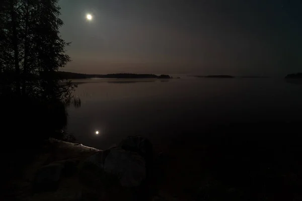 Night at full moon over the river, flowing into the lake. Silence, peace, tranquility. Large stones on the foreground.