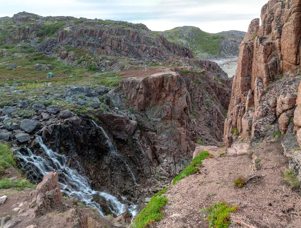 Campsite of tourists by the rocky steep shore of Barents Sea and waterfall in the tundra of the Kola Peninsula beyond the Arctic Circle — Stock Photo, Image