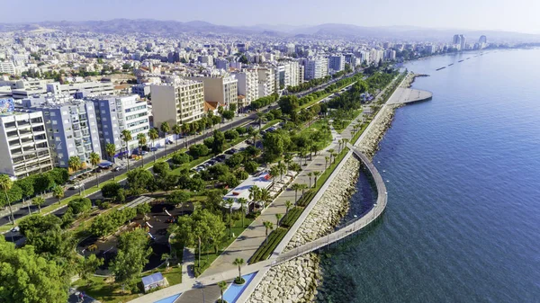 Aerial view of Molos Promenade park on the coast of Limassol city centre in Cyprus. Bird\'s eye view of the jetties, beachfront walk path, palm trees, Mediterranean sea, piers, rocks, urban skyline and port from above.