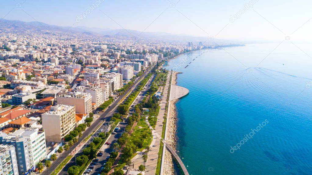 Aerial view of Molos Promenade park on the coast of Limassol city centre in Cyprus. Bird's eye view of the jetties, beachfront walk path, palm trees, Mediterranean sea, piers, rocks, urban skyline and port from above.