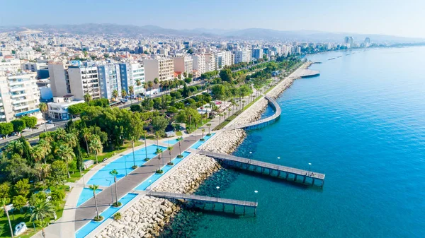 Aerial view of Molos Promenade park on the coast of Limassol city centre in Cyprus. Bird\'s eye view of the jetties, beachfront walk path, palm trees, Mediterranean sea, piers, rocks, urban skyline and port from above.