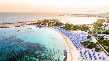 Ünlü Makronissos sahil şeridi Ayia Napa, Famagusta, Kıbrıs 'ın havadan kuş bakışı manzarası. Günbatımında Agia Napa 'da altın kum, güneşlik, deniz restoranları ve yaz tatilleri ile turistik mekan Makronisos Körfezi..